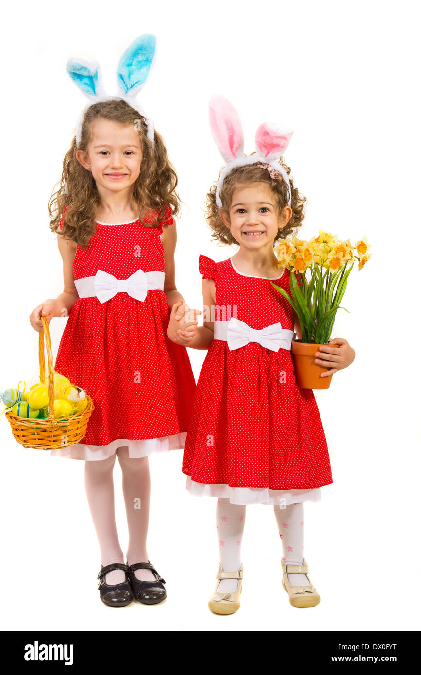 Feliz dos hermanas con orejas de conejo y las manos sosteniendo una cesta con huevos de pascua y narcisos flor aislado en blanco Foto de stock