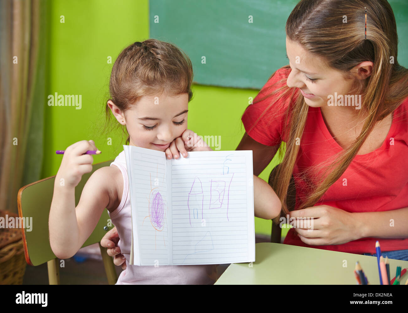Orgullosa chica mostrando su dibujo a la profesora de guardería en kindergarten. Foto de stock
