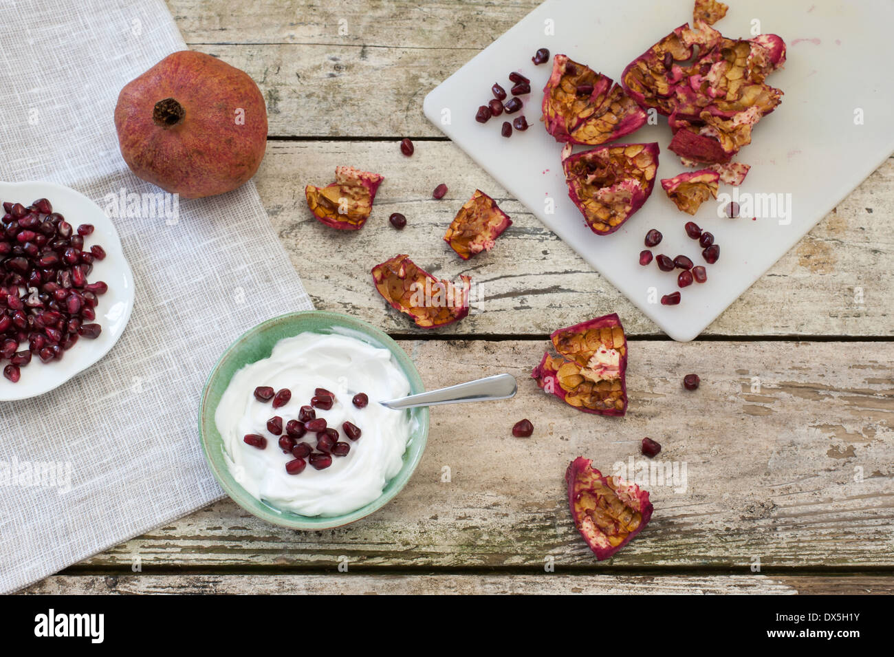 Refrigerio saludable un tazón de yogur y semillas de granada. Una fruta entera, las semillas y la piel sobre una tabla de cortar, sobre una mesa rústica Foto de stock