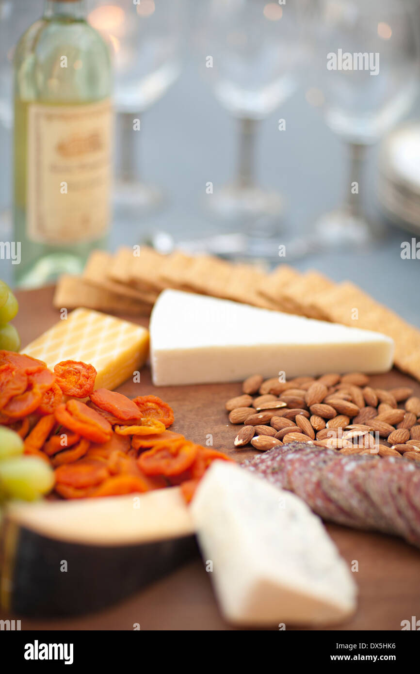 Quesos, galletas saladas, nueces, uvas y salami en tabla de quesos de madera junto al vino blanco, cerrar Foto de stock