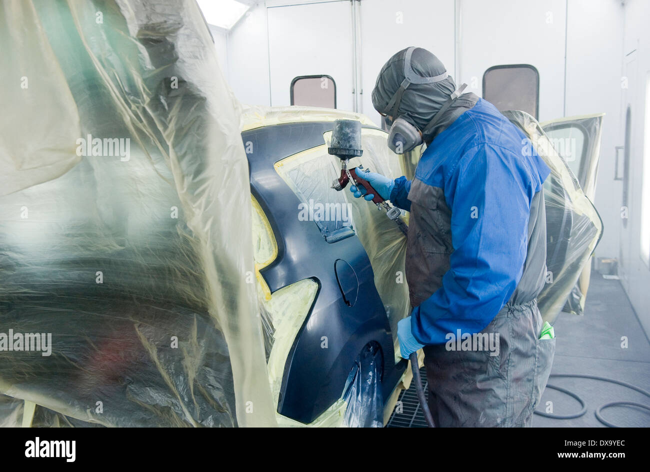 Un coche profesional pintor que está pintando la carrocería de un coche en un cuadro de pintura de un garaje con un aerógrafo. Foto de stock