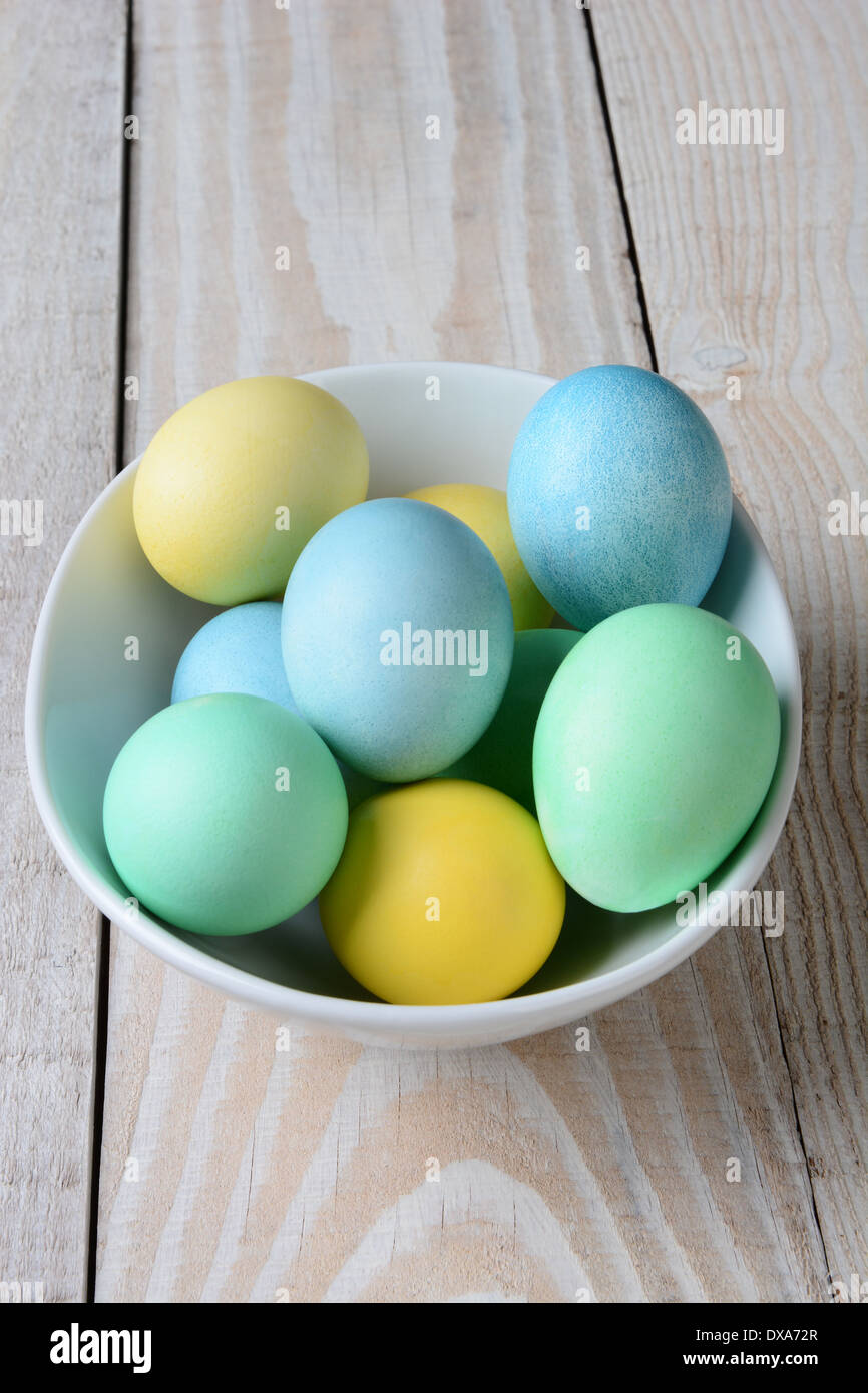 Un alto ángulo de visualización de huevos de Pascua pastel en un tazón. El tazón blanco está lleno de amarillo, verde y azul huevos teñidos Foto de stock