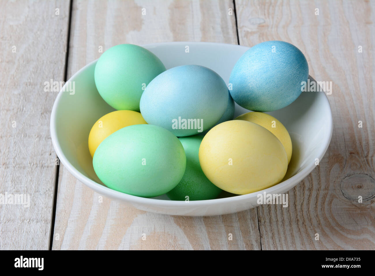Un alto ángulo de visualización de un tazón de pastel de huevos de Pascua. El tazón blanco está lleno de amarillo, verde y azul huevos teñidos Foto de stock