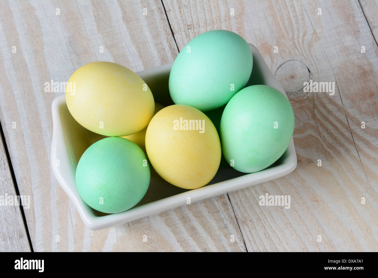 Un alto ángulo de visualización de un recipiente rectangular de pastel de huevos de Pascua. El tazón blanco está lleno de huevos teñidos de verde y amarillo Foto de stock