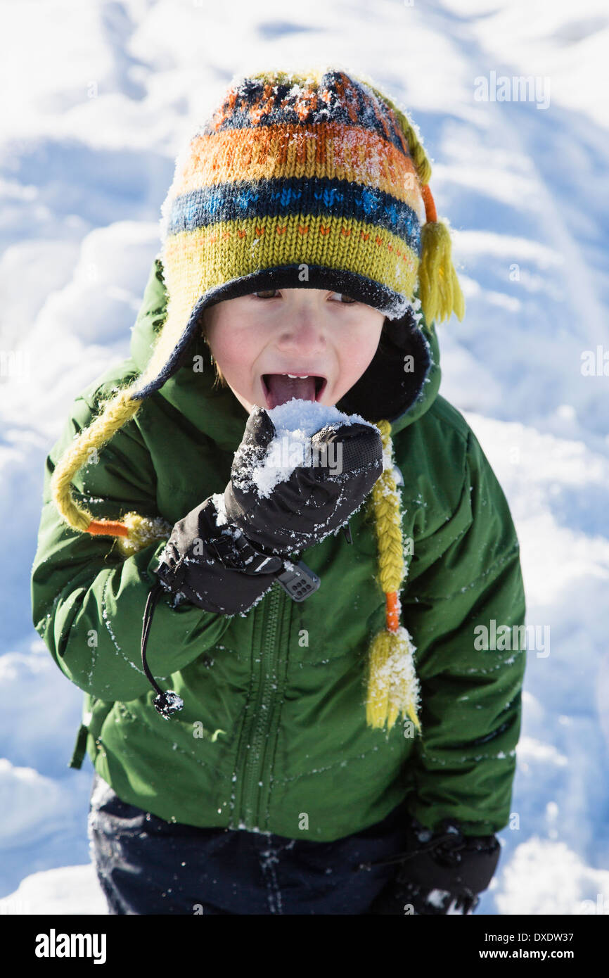 Niño vestido con guantes hinchados para la nieve y un gorro colorido  tratando de atrapar copos de nieve en su lengua con una enorme sonrisa  contagiosa