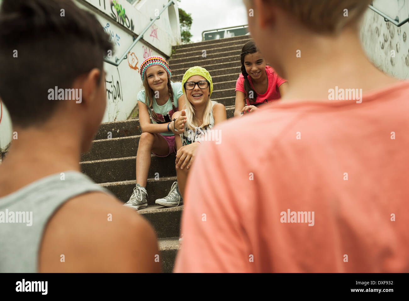 Backview de dos chicos hablando a las niñas sentadas en las escaleras exteriores, Alemania Foto de stock