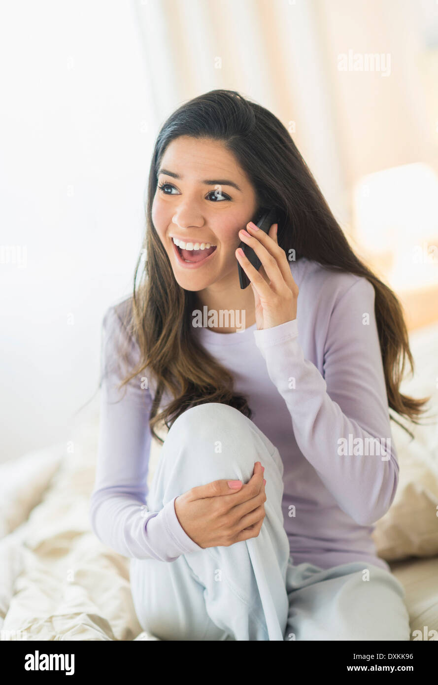 Mujer Hispana entusiasta hablando por teléfono celular en la cama Foto de stock
