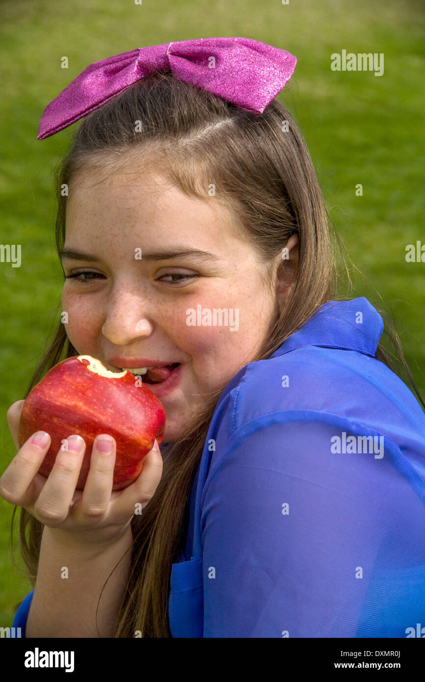 Un feliz joven chica caucásica comiendo una manzana Gala al aire libre en un Lagnua Beach, CA, y estacionamiento. Foto de stock