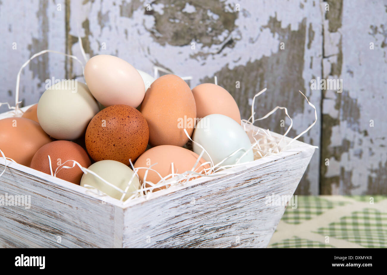 Surtido de color diferente, fresco, huevos de gallina en un contenedor de madera estilo country, fondo de cocina Foto de stock