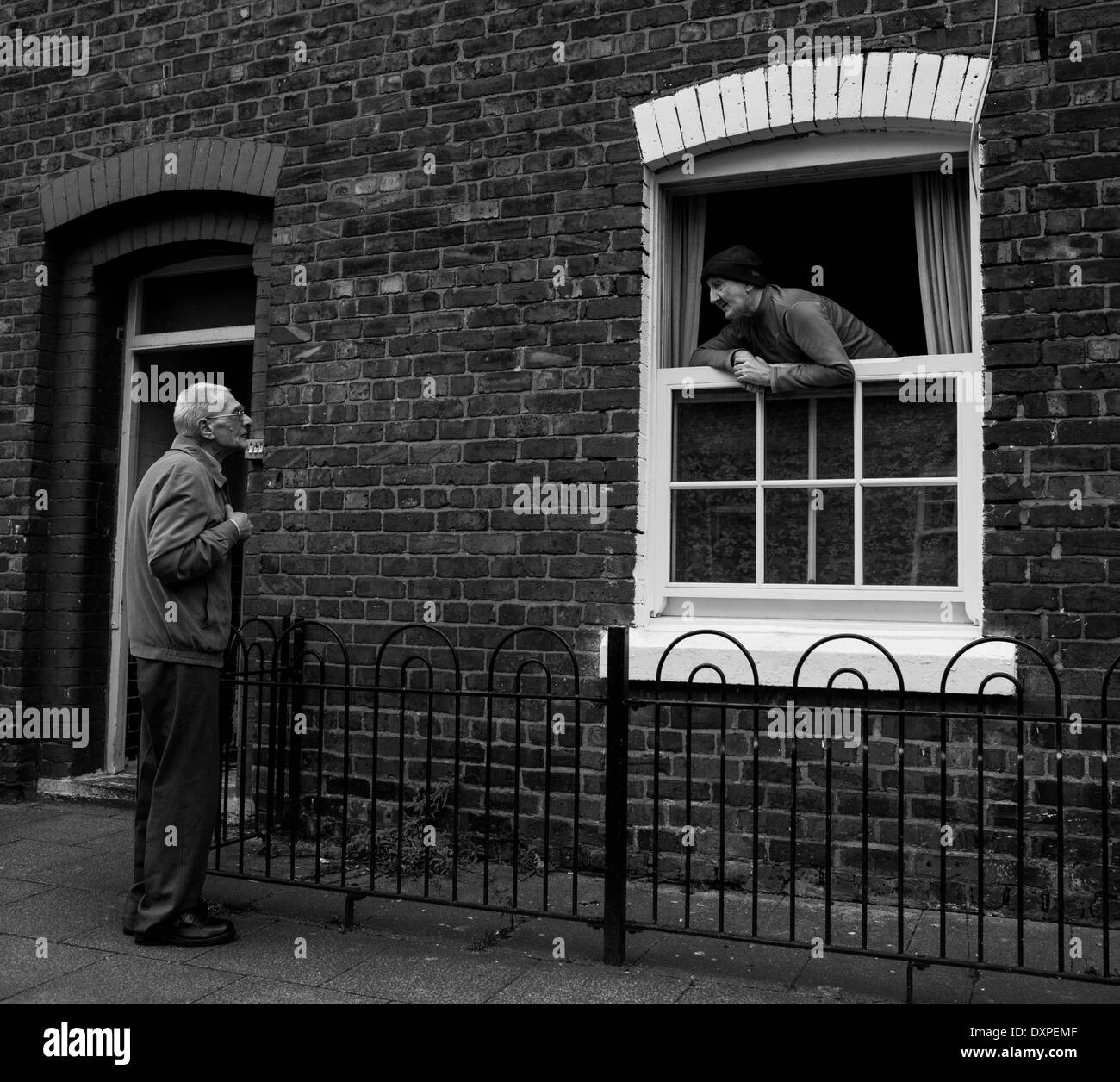 Vecinos conversando sobre la valla de una casa de ladrillo. Foto de stock