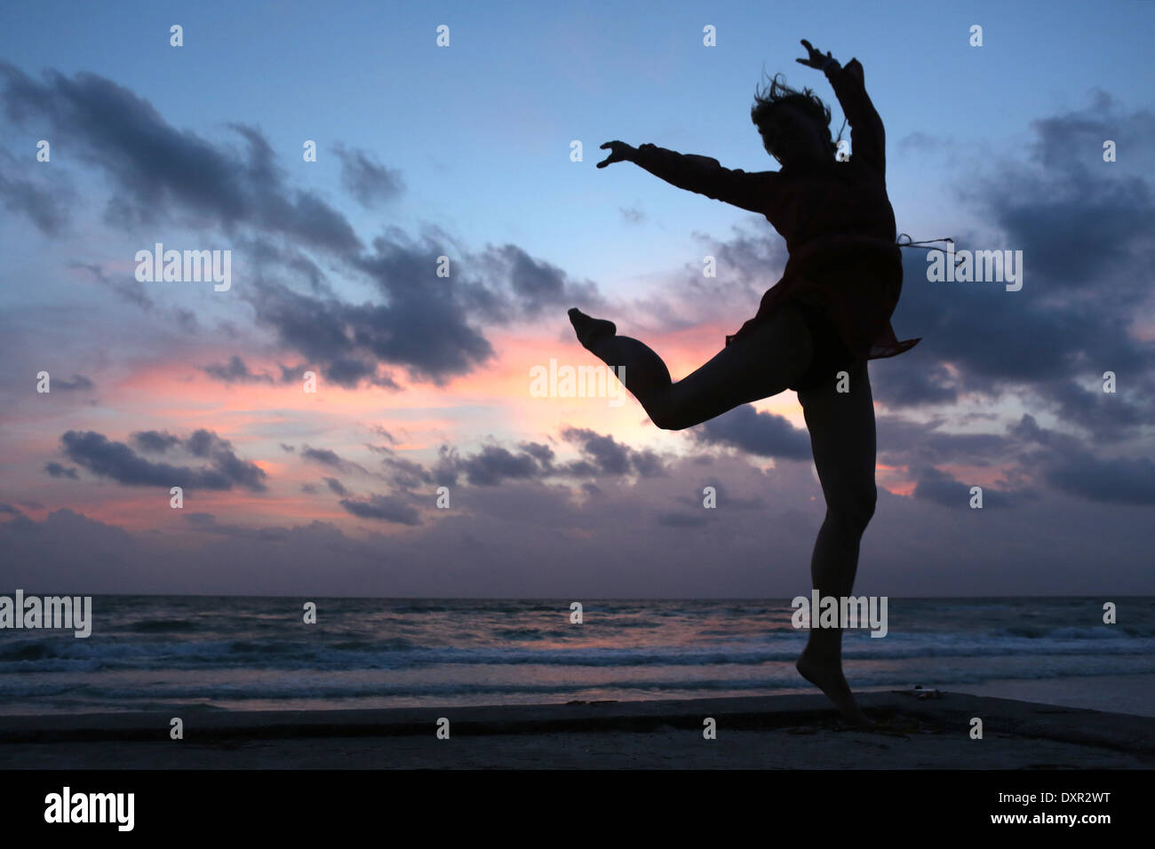 Pasar una rejilla, Estados Unidos de América, la silueta, la mujer está haciendo un salto en el aire al atardecer en la playa Foto de stock