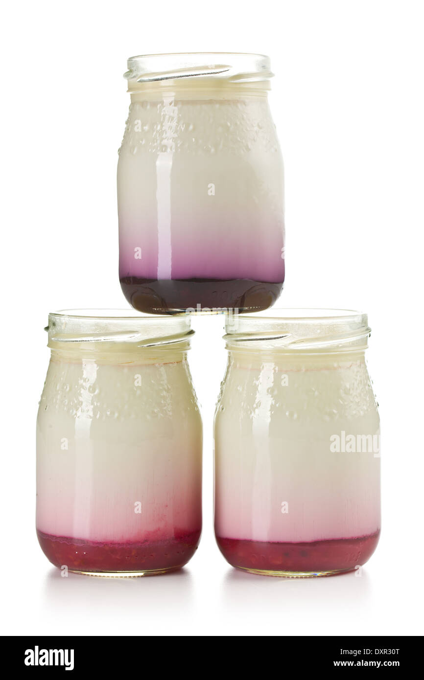 Tres frascos con yogur frutado sobre fondo blanco. Foto de stock
