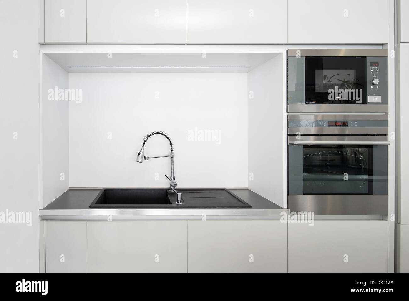 Cocina amueblada con una combinación de muebles en blanco y negro sin  tiradores visibles y con electrodomésticos negros y grifería del mismo  color Fotografía de stock - Alamy