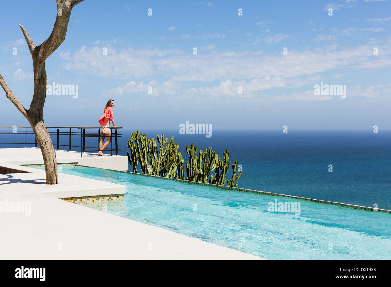 Mujer de pie al lado de la piscina en el balcón con vistas al mar Foto de stock
