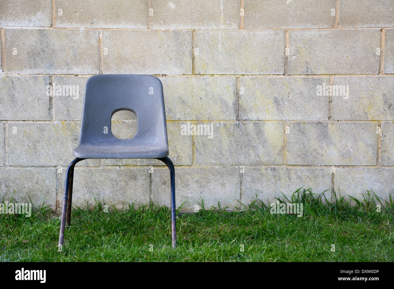 Silla de plástico vacías abandonadas sobre el césped delante de una pared de bloques de concreto Foto de stock
