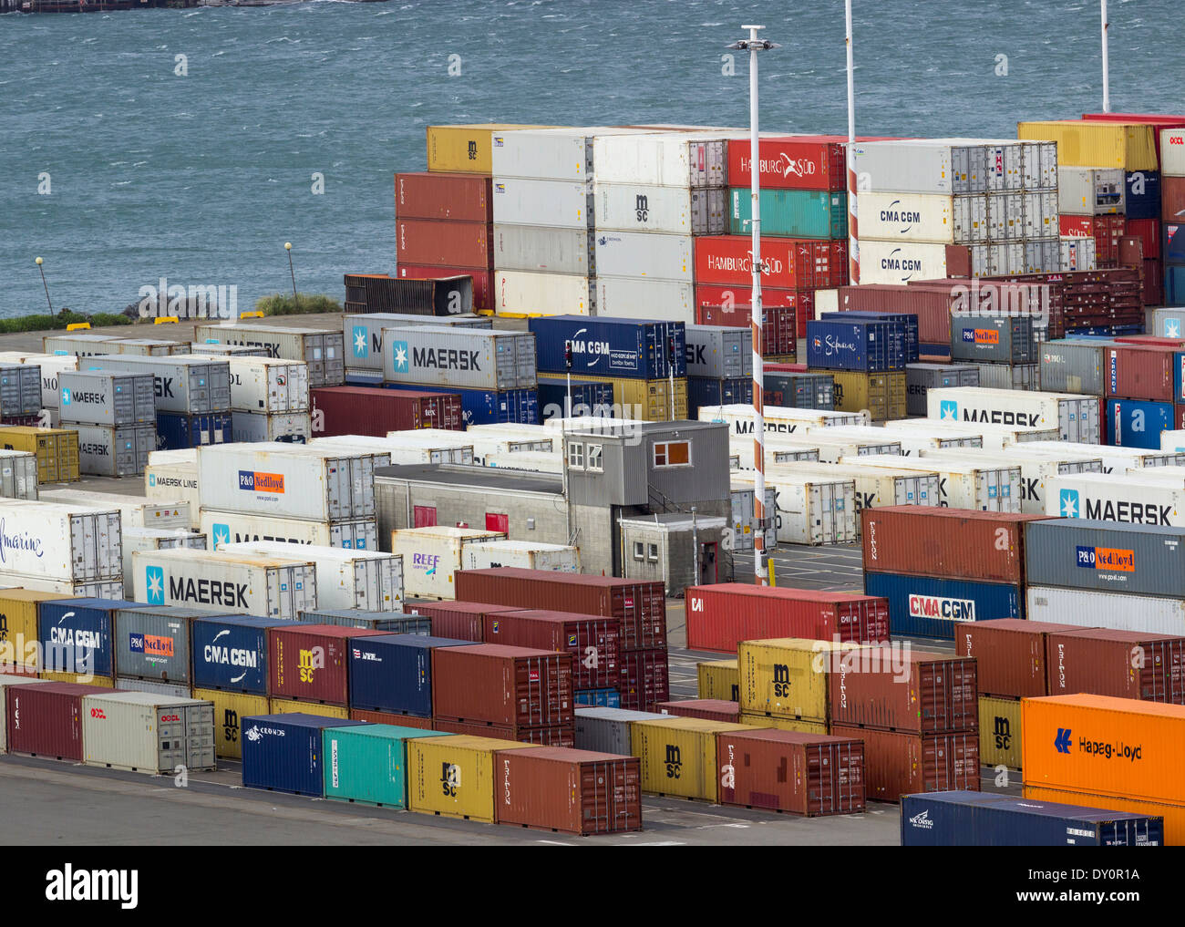 Las pilas de contenedores industriales por un muelle en un puerto Foto de stock
