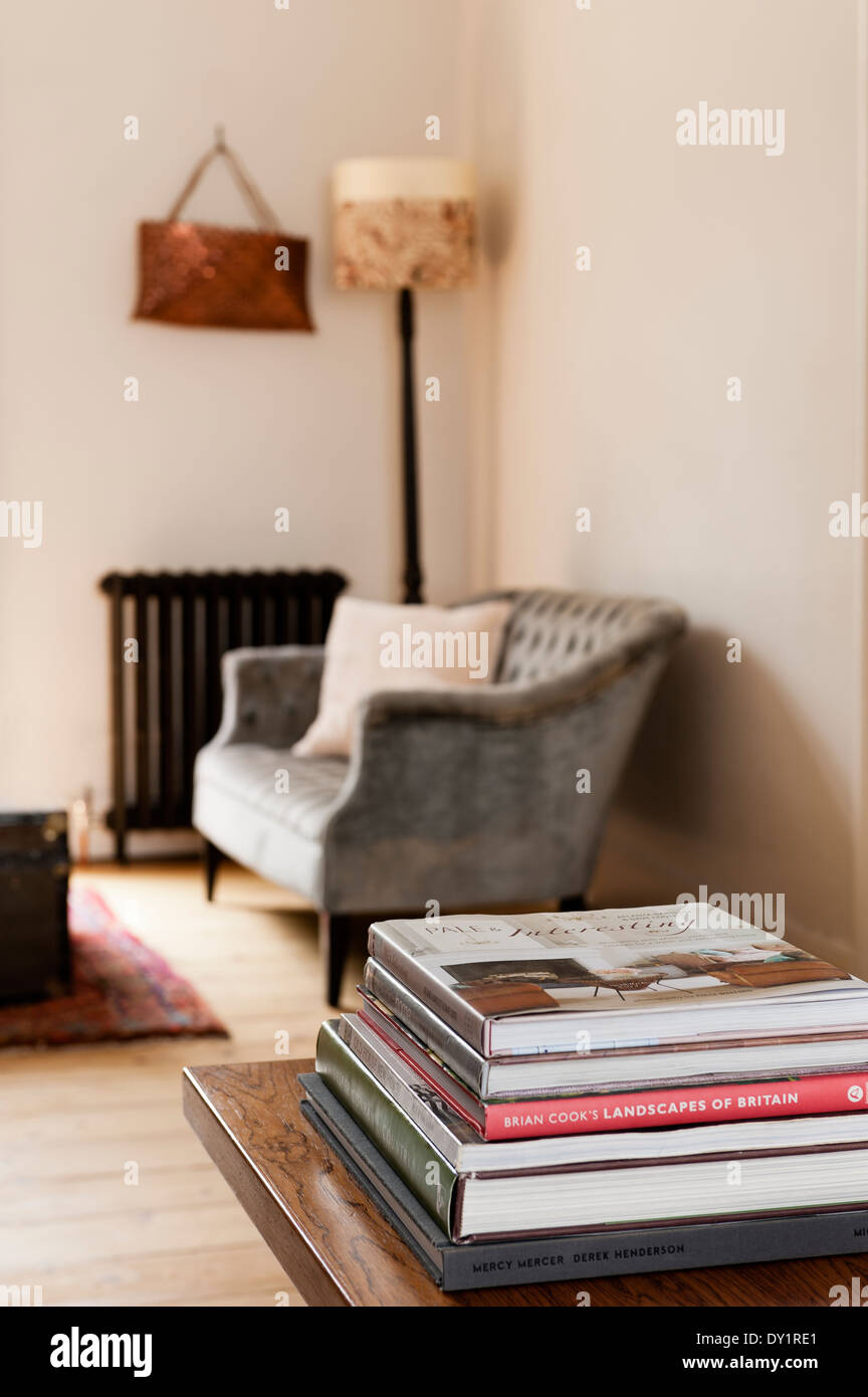 Pila de libros sobre una mesa de café en madera con sofá y seguro en el fondo del radiador antiguo Foto de stock