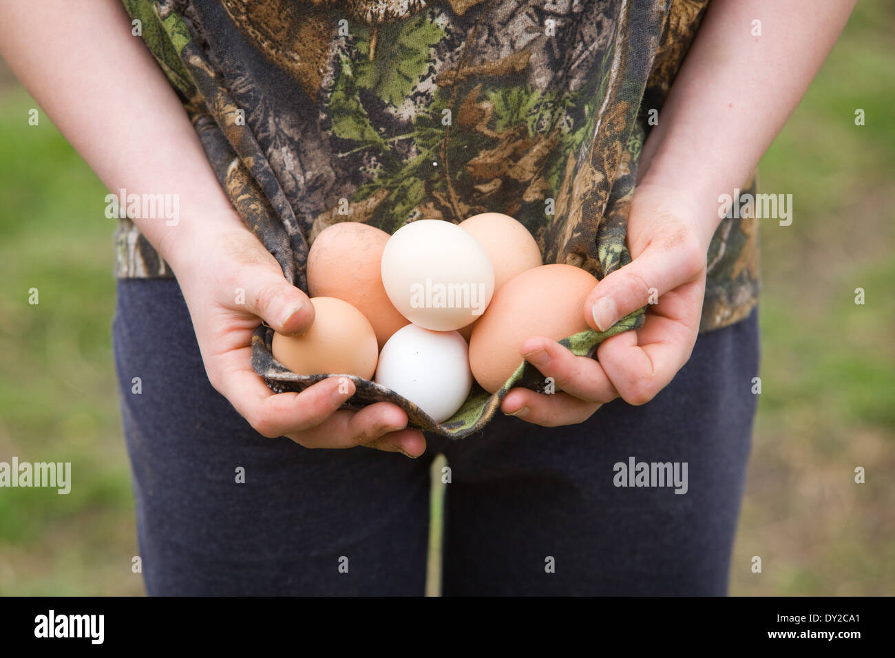 Un niño fuera y sosteniendo una selección de huevos de gallina en su t-shirt Foto de stock