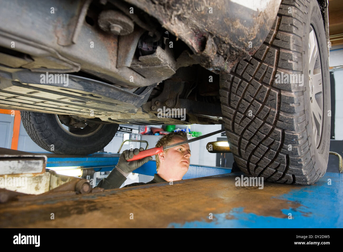 Un técnico está comprobando el estado técnico debajo de un coche levantado sobre un puente en un garaje Foto de stock