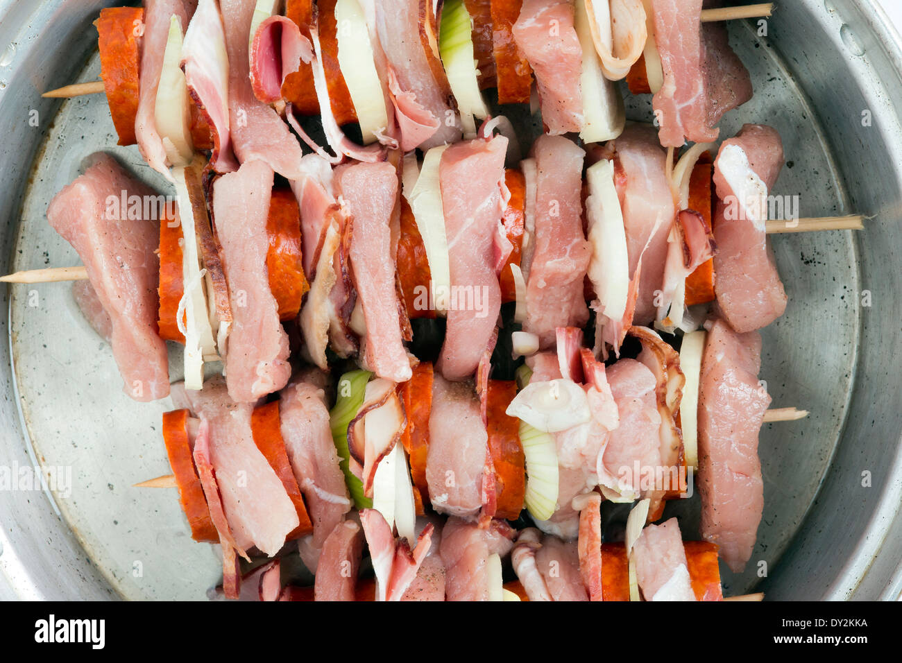Brochetas de carne de cerdo cruda - mezcla de carnes, salchichas y cebollas. Foto de stock
