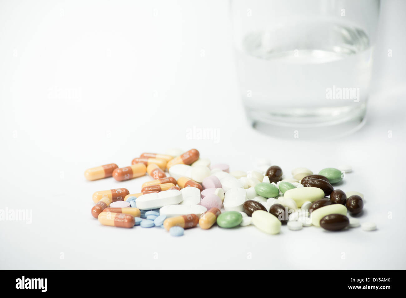 Píldoras cerca de una taza de agua sobre fondo blanco. Foto de stock