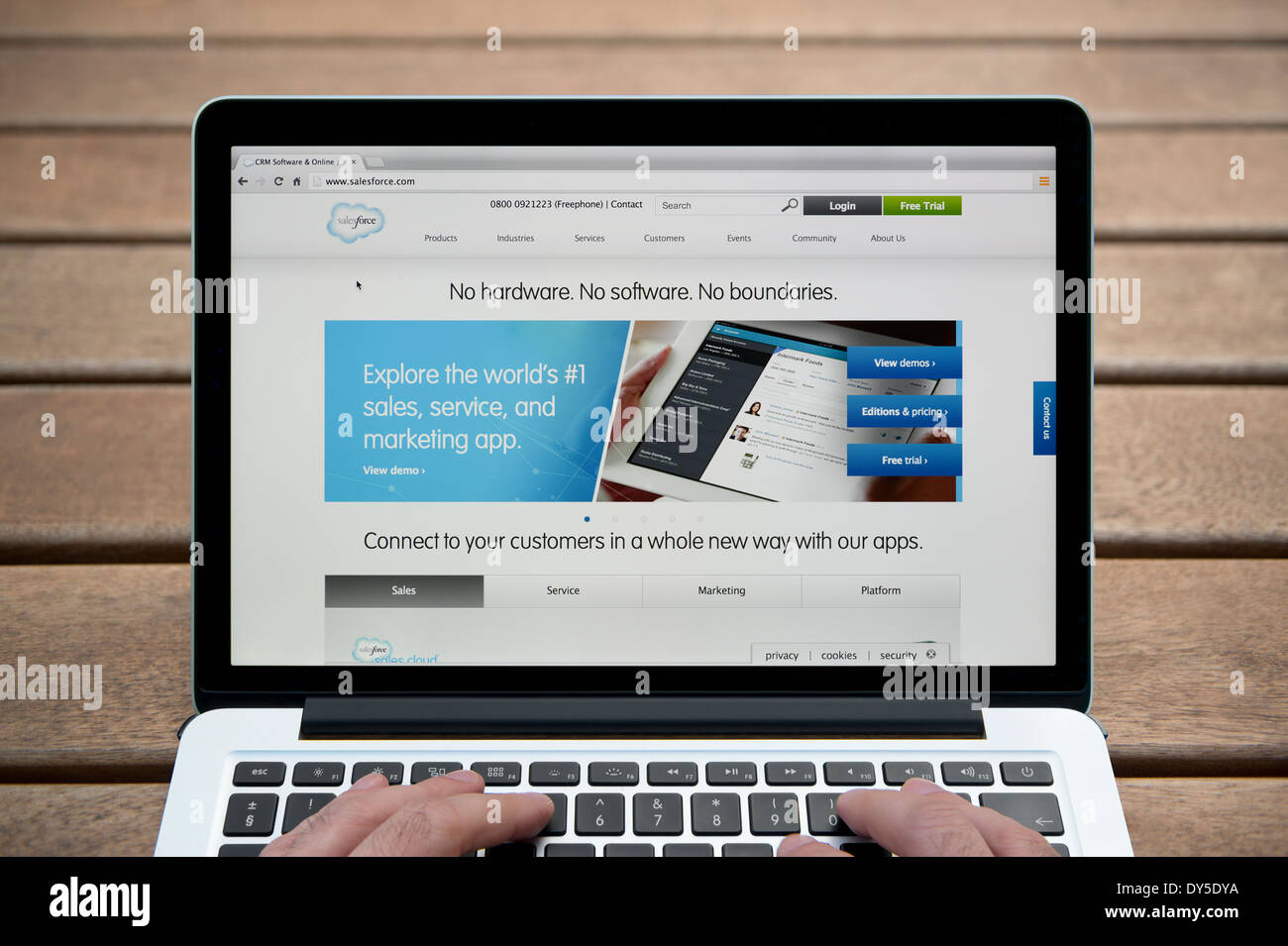 El sitio web de la fuerza de ventas de MacBook contra un banco de madera de fondo al aire libre incluyendo un hombre de dedos (uso Editorial solamente). Foto de stock