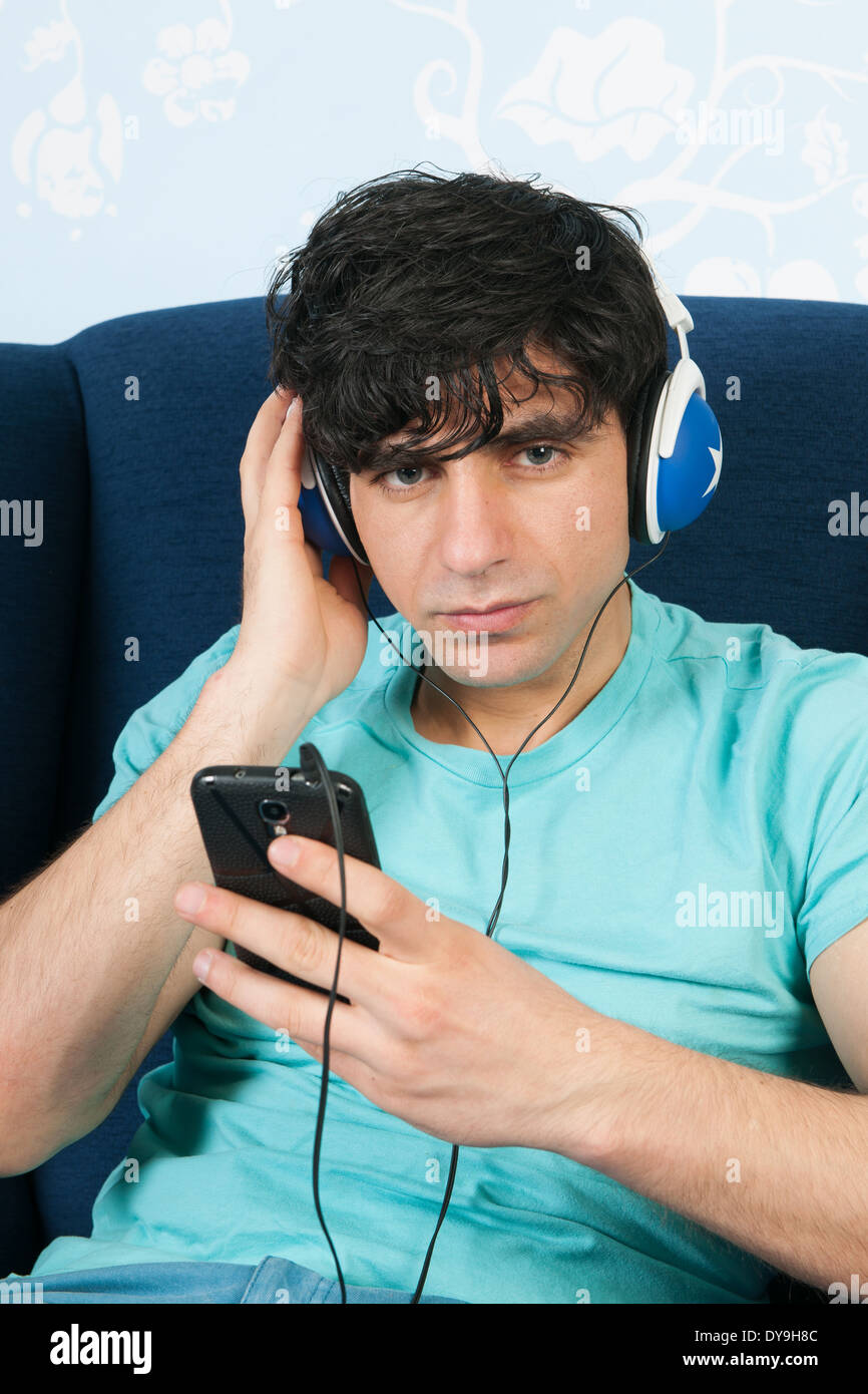 Hombre joven sentado en el living escuchando música con el teléfono inteligente. Foto de stock