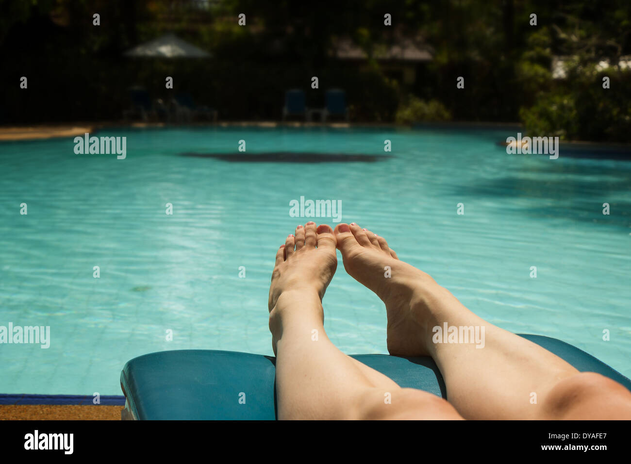 Primer plano de los pies de una mujer para tomar el sol en tumbonas junto a la piscina Foto de stock