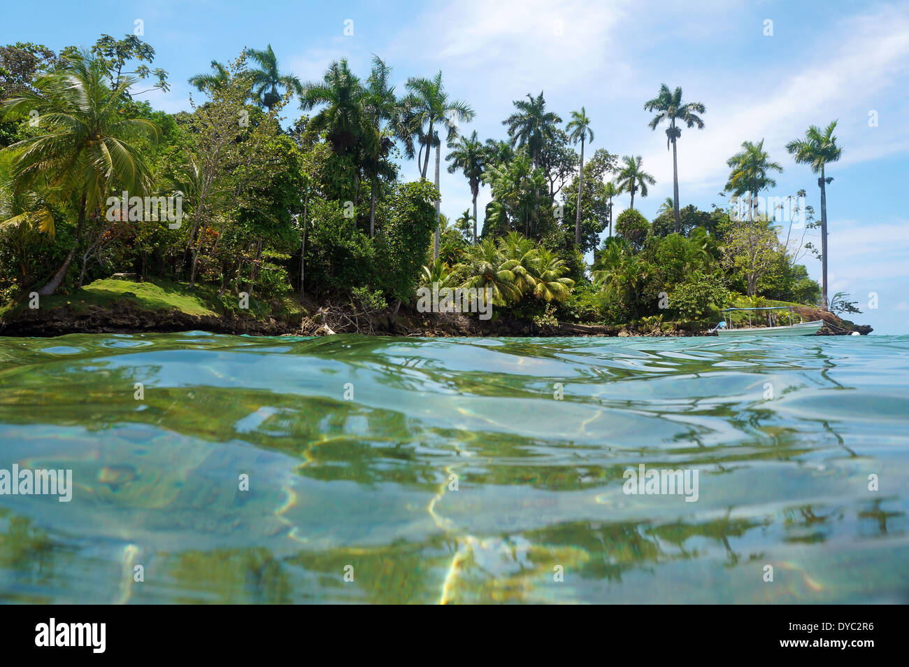 Isla tropical con vegetación exuberante y un barco en la boya de amarre, visto desde la superficie del agua del mar Caribe, Panamá Foto de stock