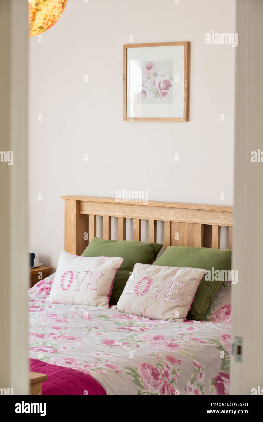 Una imagen de estilo de vida de una cama en un dormitorio con almohadas bordadas con la palabra amor a ellos y una rosa imprimir cubrecama Foto de stock
