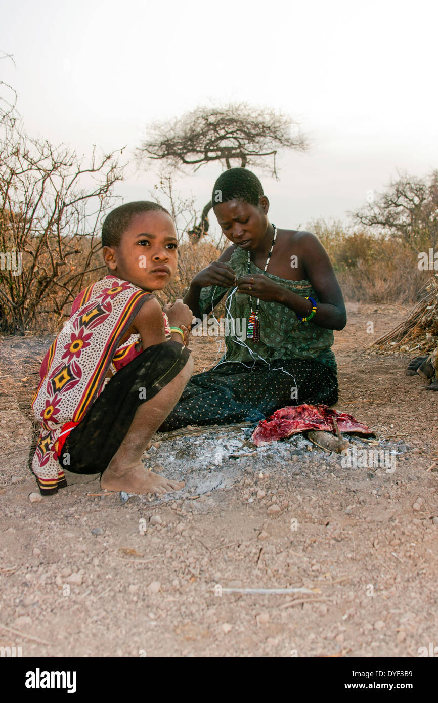 Mujer y Niño hadzabe, secado de carne en un incendio. Fotografiado en Tanzania, el lago Eyasi Foto de stock