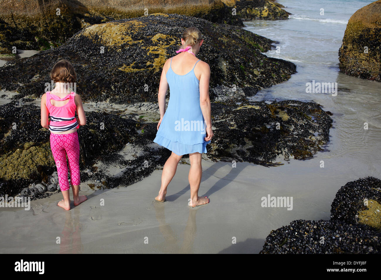 Madre e hija buscando animales en pequeñas piscinas en la roca por el mar. Langebaan, Western Cape. Foto de stock