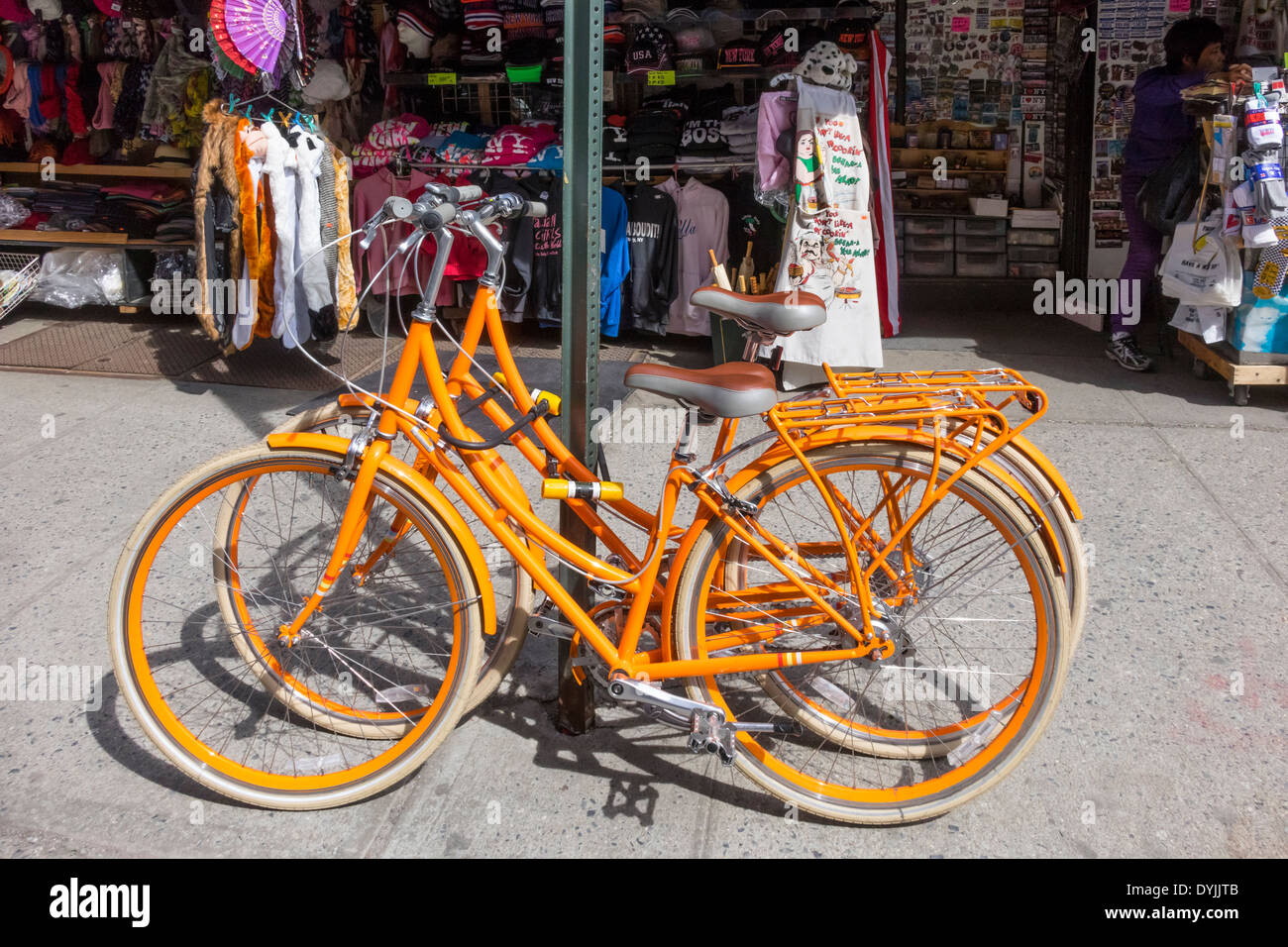 Coincide la mujer bicicletas naranja en frente de una tienda de venta de artículos para turistas en la calle Mulberry en Little Italy en NYC Foto de stock