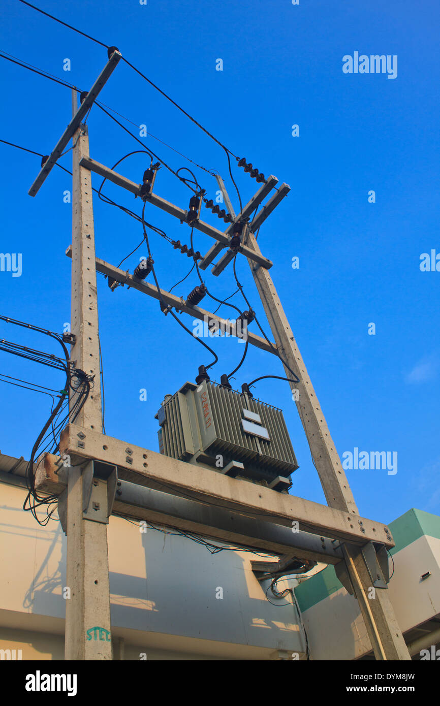 Los transformadores de un poste eléctrico con líneas de energía contra el cielo azul brillante Foto de stock