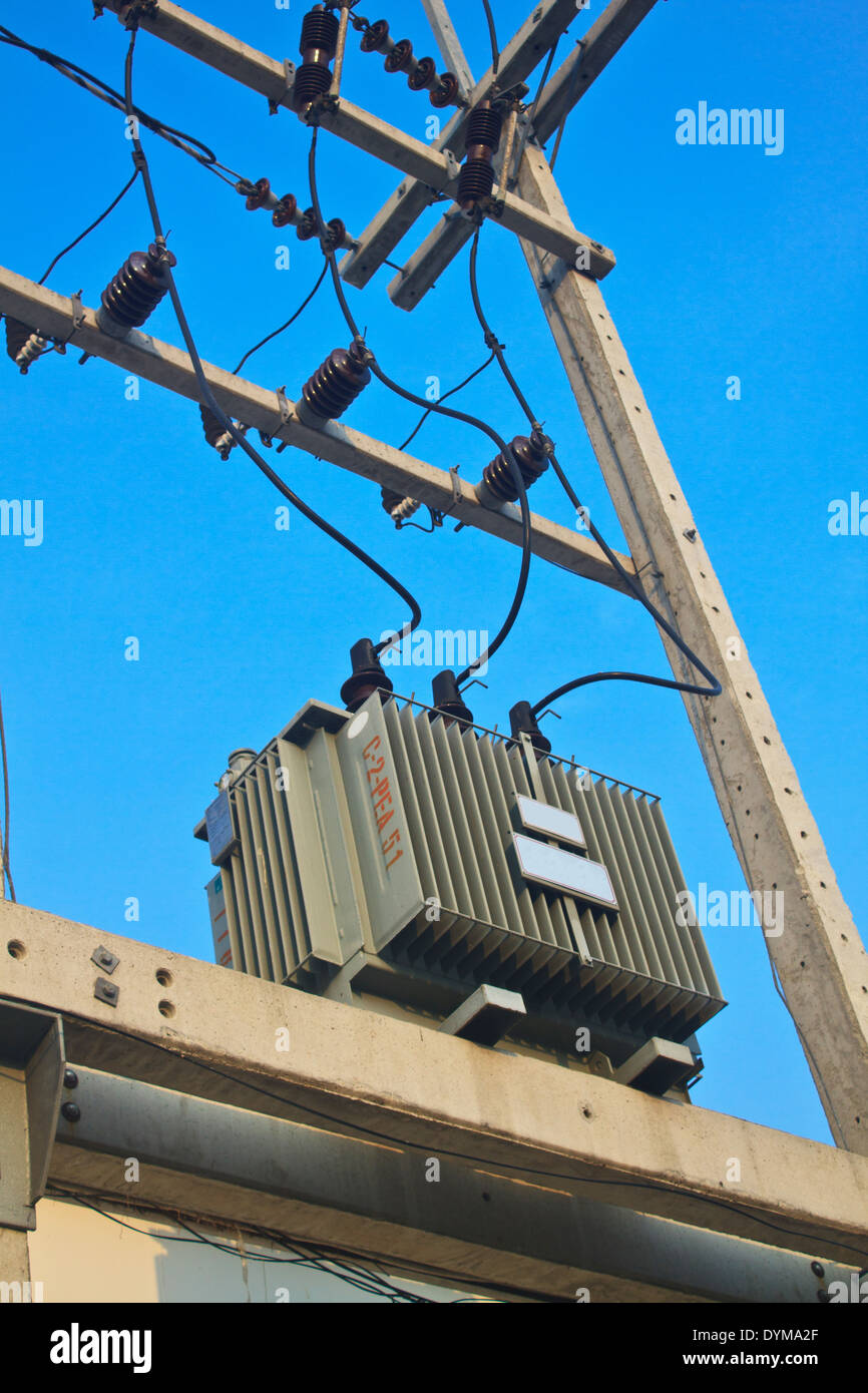 Los transformadores de un poste eléctrico con líneas de energía contra el cielo azul brillante Foto de stock