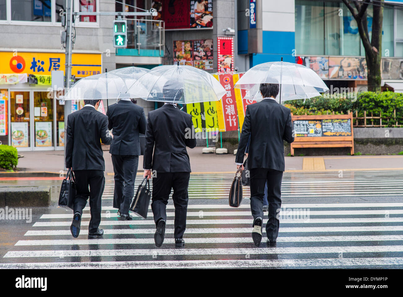 Los trabajadores japoneses machos adultos bien vestidas con sombrillas cruzando la calle, Shinjuku, Tokio, Japón Foto de stock