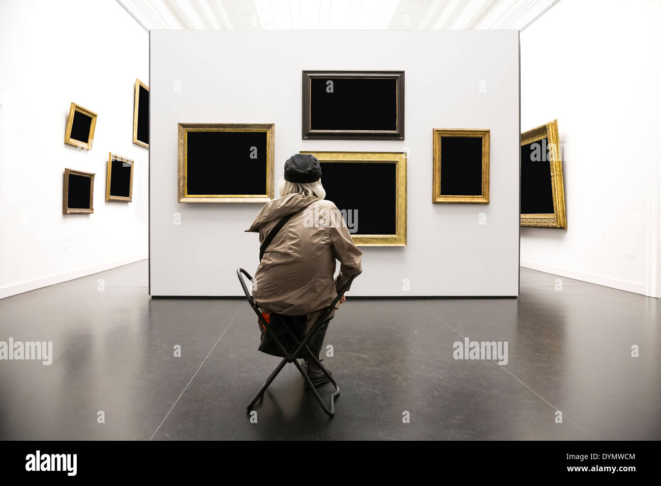 La vieja señora se sienta delante de una pared con pinturas en galería de arte Foto de stock