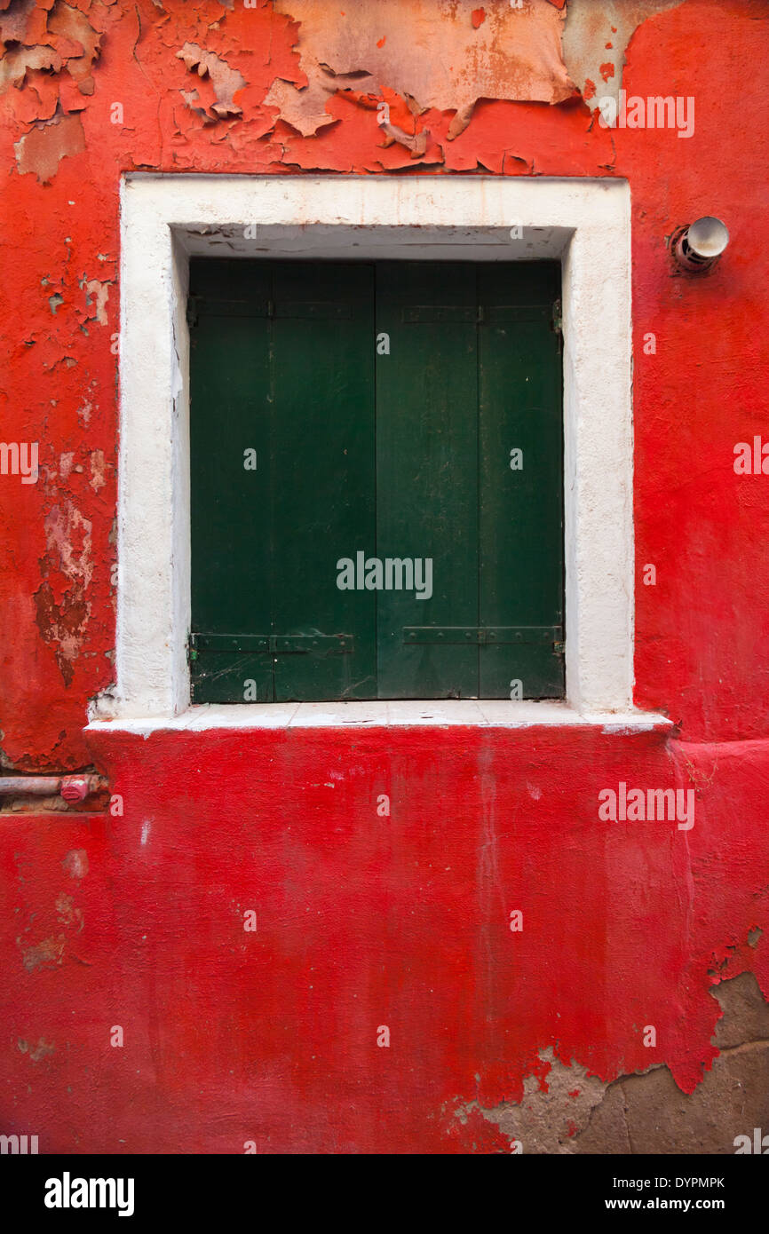 Vertical cerca de la ventana con persianas verdes sobre la pared de color rojo brillante, Venecia Foto de stock