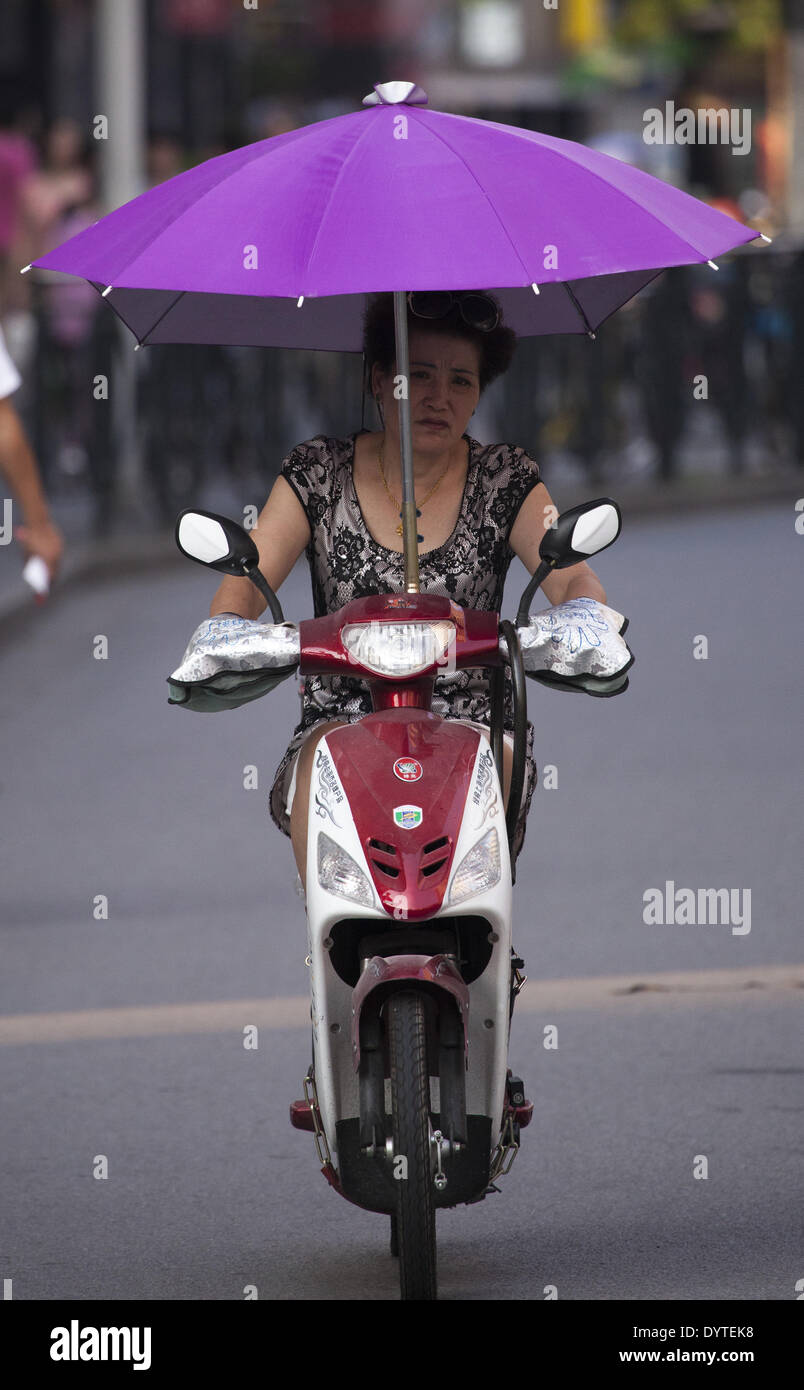 Una mujer en una bicicleta eléctrica utiliza un paraguas protector para el  calor Fotografía de stock - Alamy