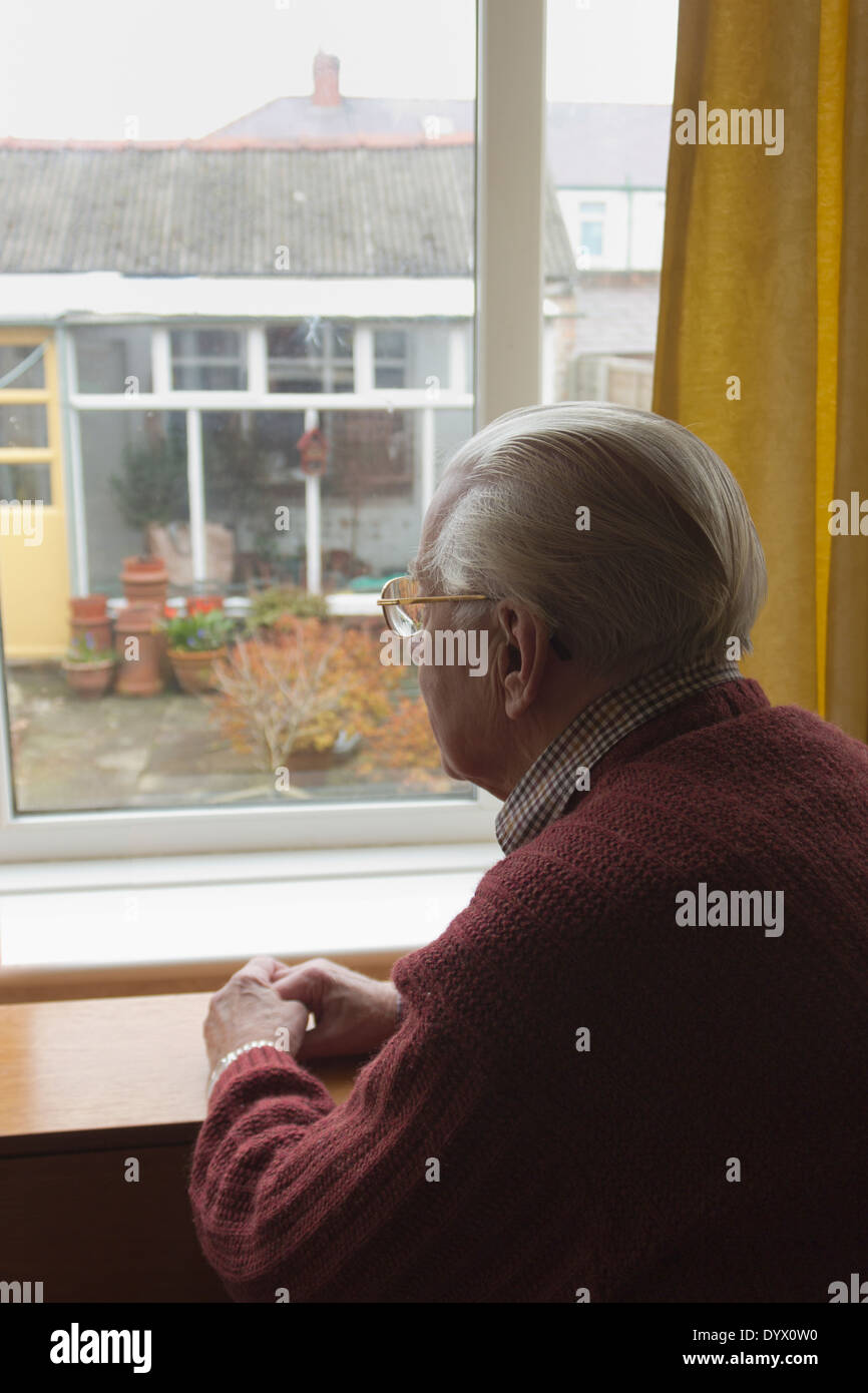 Solitario hombre viejo mirando hacia afuera de la ventana al jardín. Foto de stock