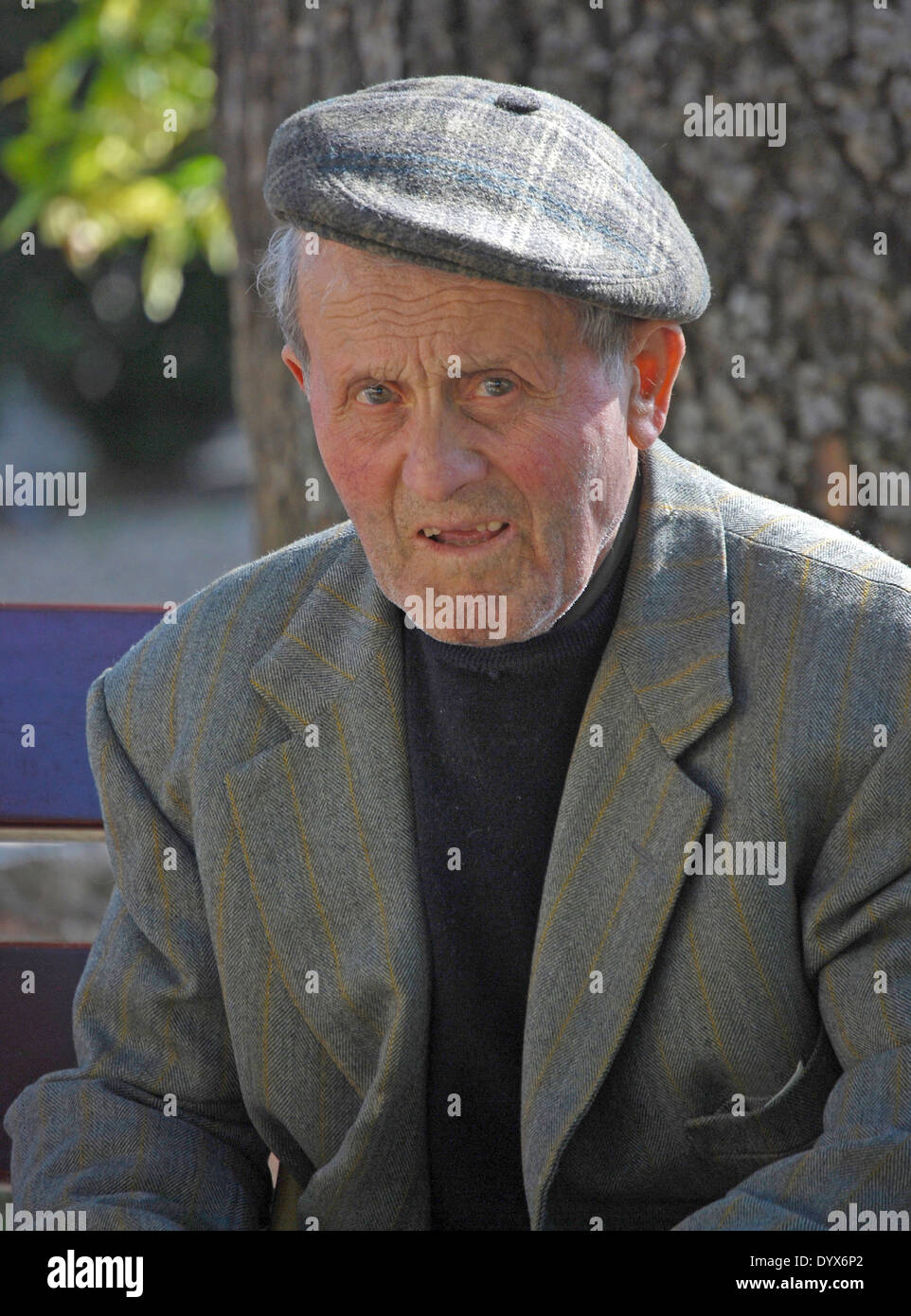 Pienza, Italia. Retrato de un hombre mayor de edad en una gorra sentado en una banca del parque. Foto de stock