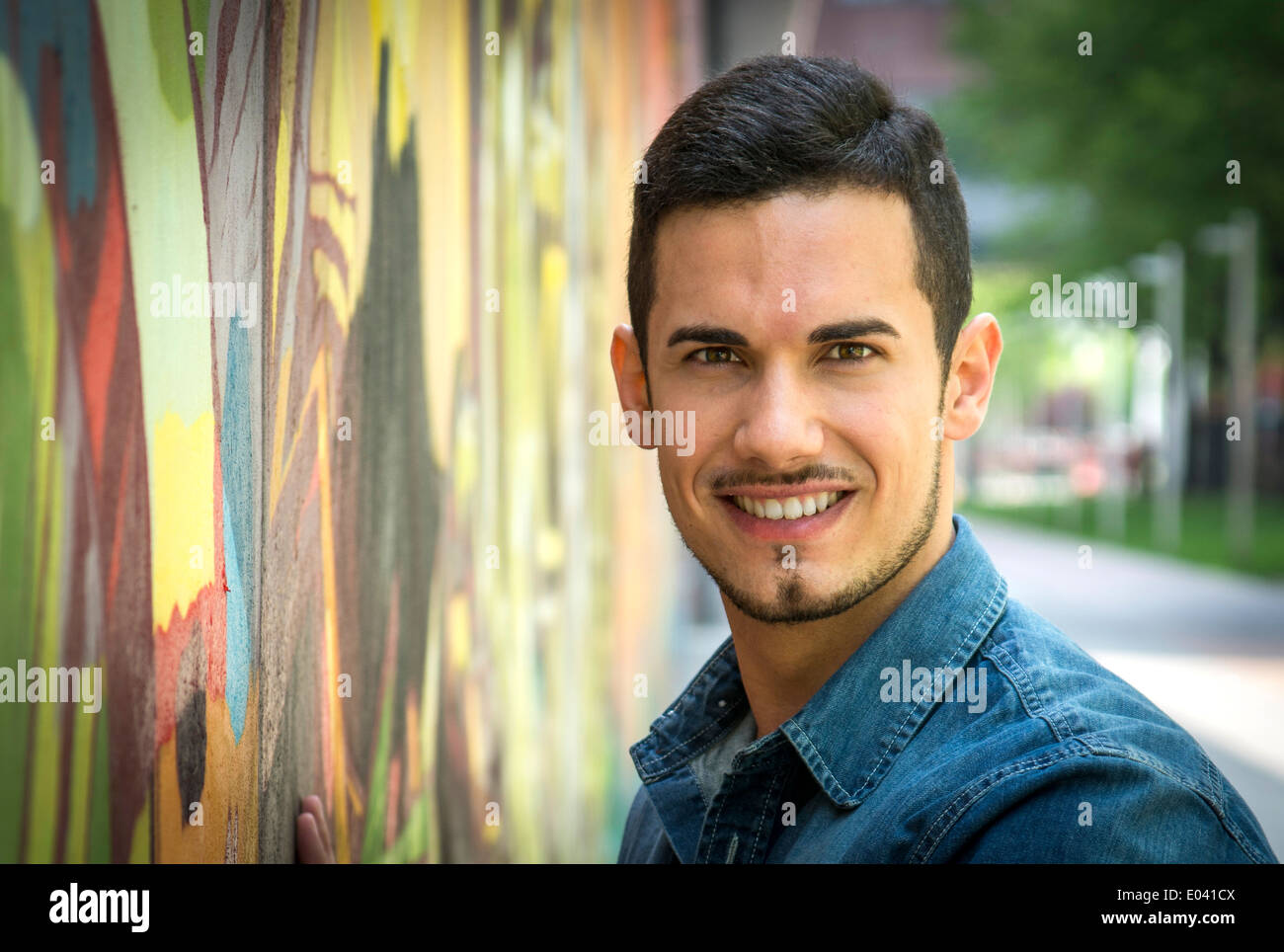 Joven sonriente junto al colorido graffiti wall, mirando a la cámara Foto de stock