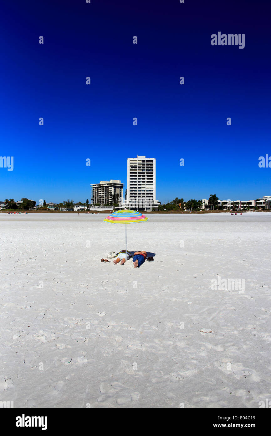 Una pareja irreconocible bajo una sombrilla recostada sobre la arena en Siesta Key Beach en Sarasota, Florida, EE.UU. Foto de stock