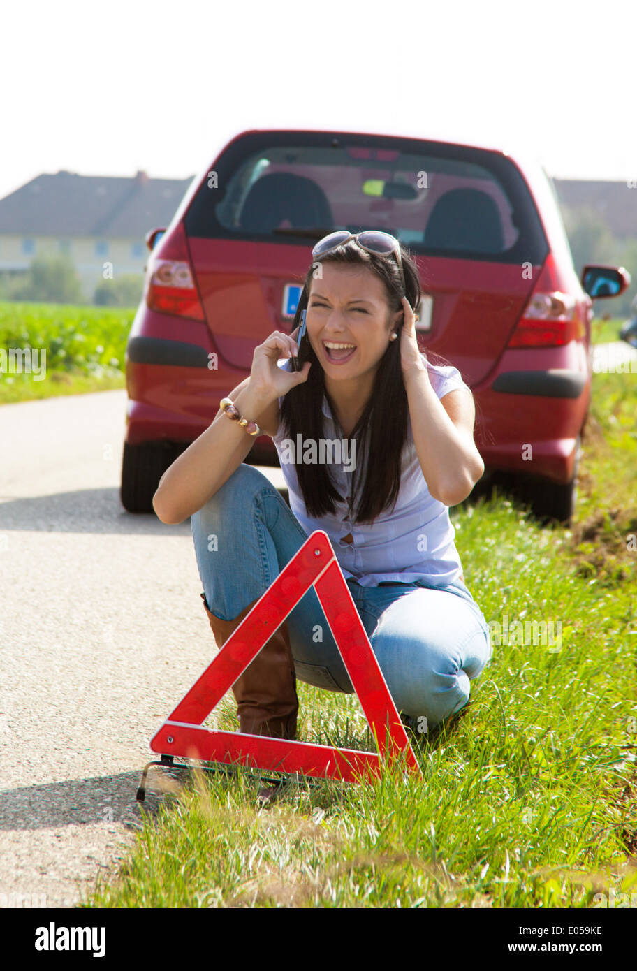 Mujer joven con un triángulo de advertencia con un desglose, Junge Frau mit einem Warndreieck bei einer Panne Foto de stock