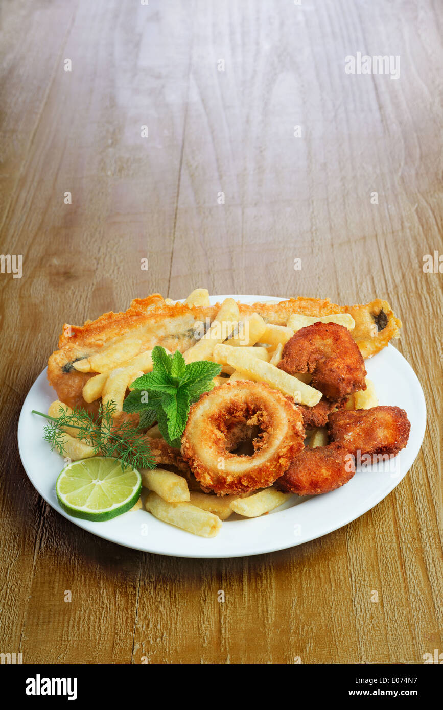 Plato de marisco crumbed con pescado, calamares, gambas y patatas fritas en vintage tabla Foto de stock