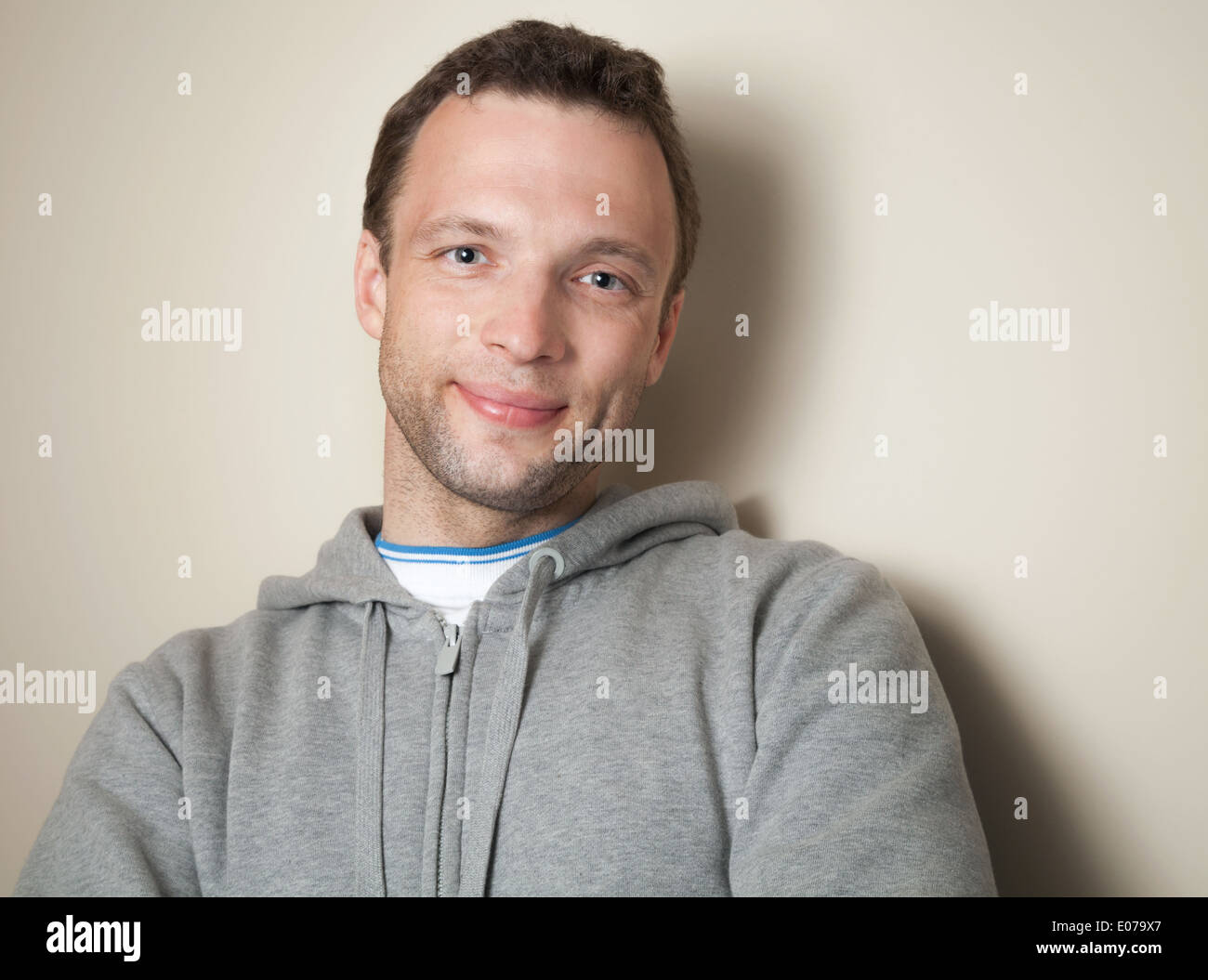 Joven Hombre caucásico positivo en gris chaqueta deportiva con capucha Foto de stock