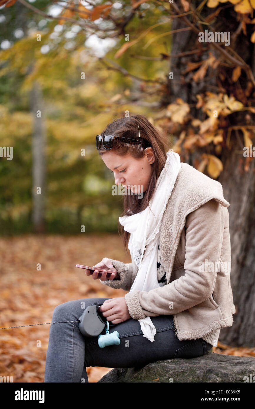 Vista lateral de la joven mujer leyendo el mensaje de texto en el teléfono inteligente en el bosque Foto de stock