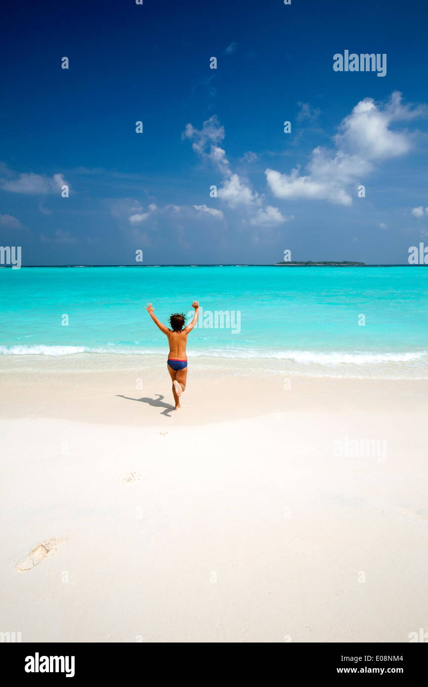 Niño corriendo con los brazos levantados en playa tropical, Maldivas, Océano Índico, Asia Foto de stock