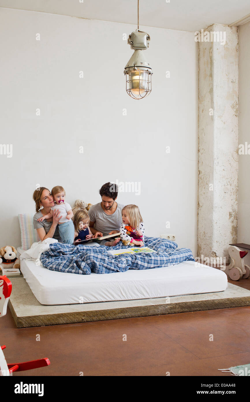 Familia con tres hijas leer libros en la cama Foto de stock