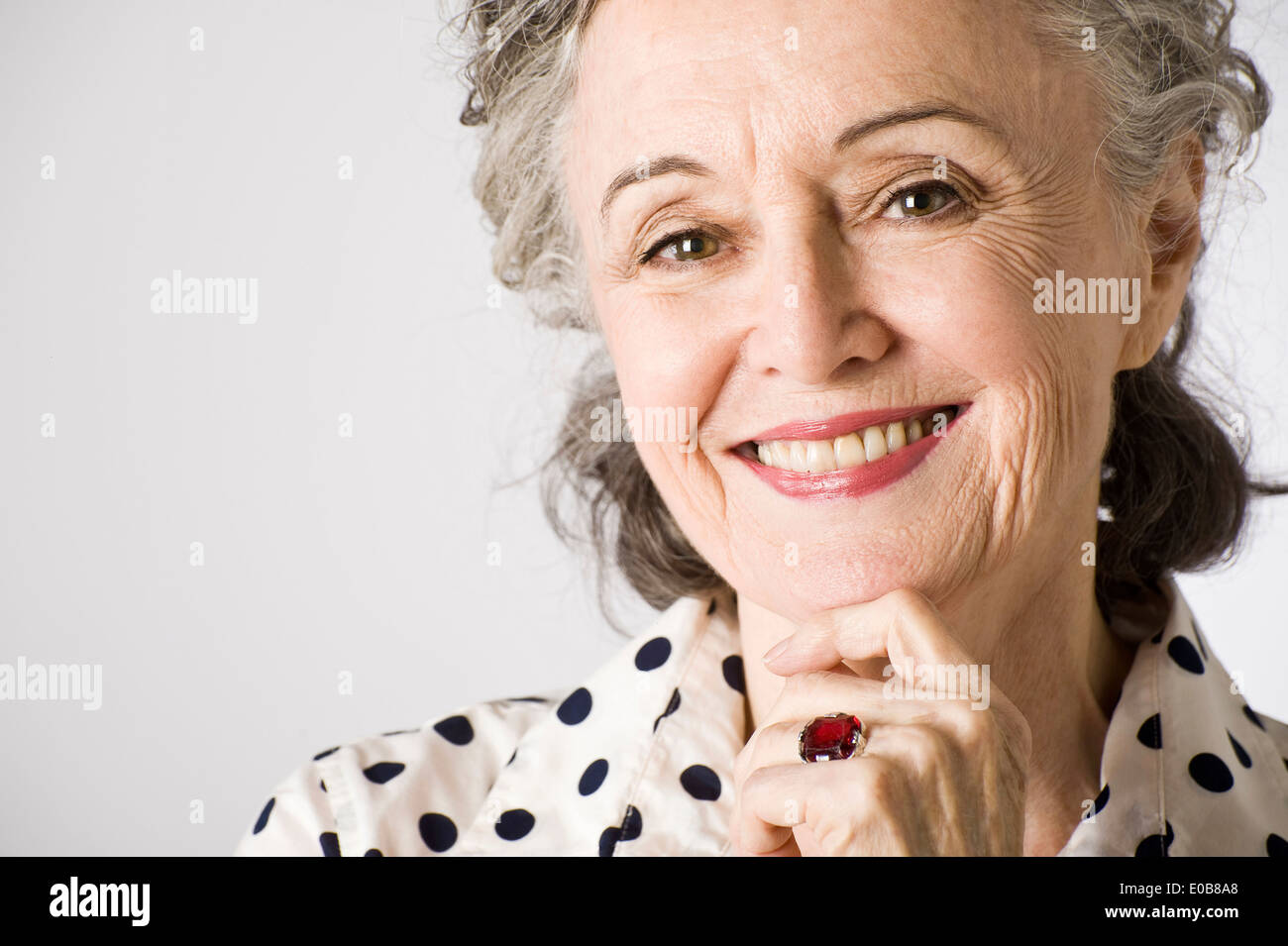 Retrato de mujer mayor, con la mano en el mentón, sonriendo Foto de stock